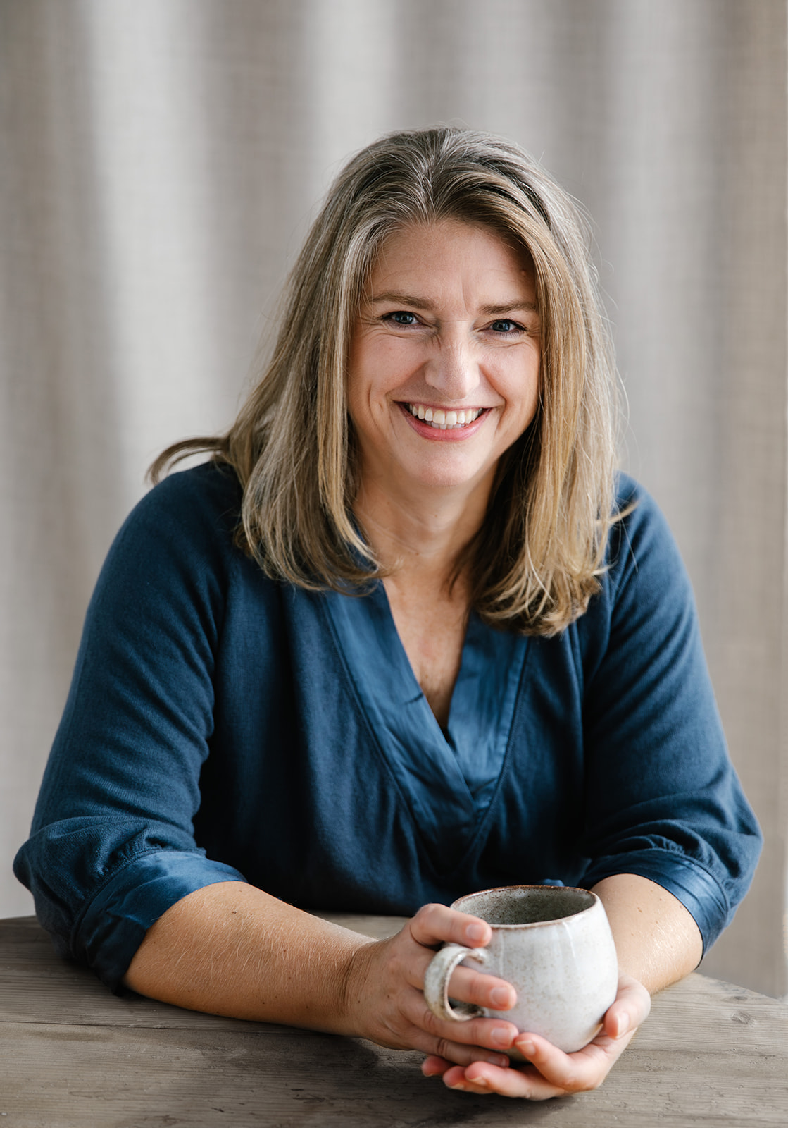 Annika Telléus sitting at a wooden table holding a ceramic cup